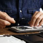 Serviser mobilnih telefona pincetom popravlja rastavljen telefon na radnom stolu