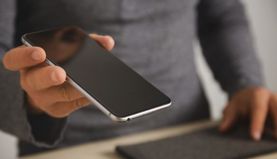 Osoba drži mobilni telefon sa ugašenim ekranom pre predaje uređaja na servis